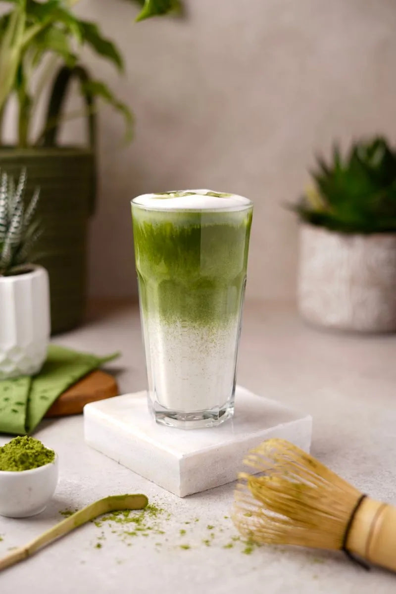 An iced matcha latte on a marble slab surrounded by greenery